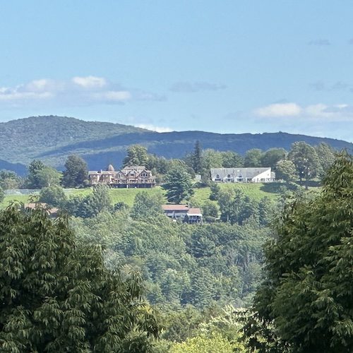 The Winden Hill Condominium, atop a distant hill, nestled among trees, shadowed by a bright but cloudy sky